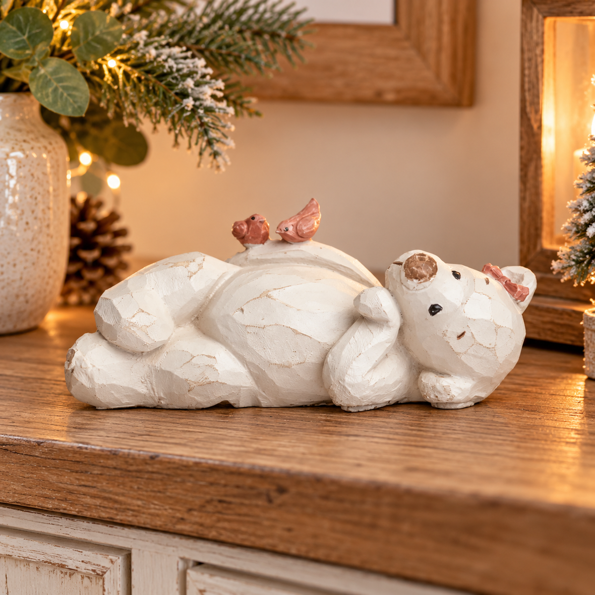 Daisy cream resin bear ornament lying on her back with two pink birds, displayed on a wooden sideboard in a cosy home.