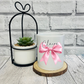 Personalised white ceramic pen pot featuring a pink satin bow design and custom name in black script.
